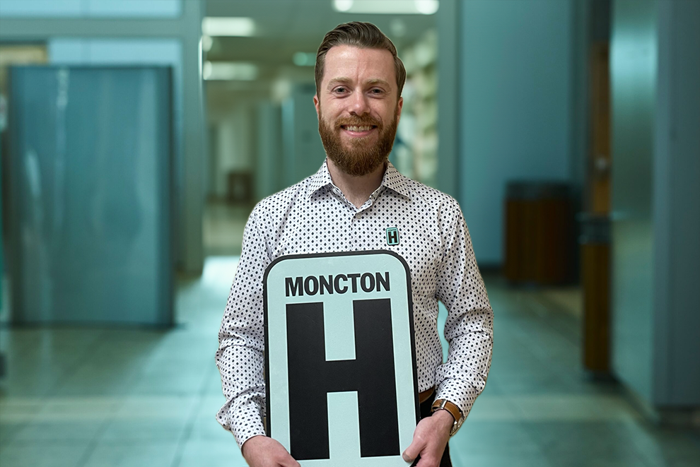 Aaron McLean Holding H Sign and Smiling at camera