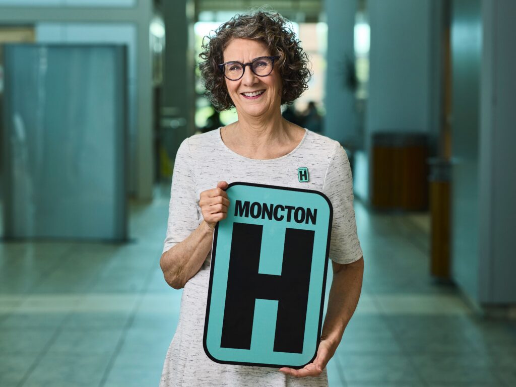 Celine Robichaud Holding H Sign and Smiling at camera