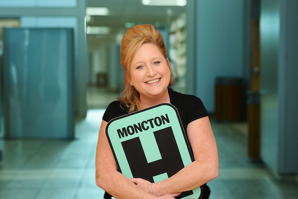 Marianne Mepham-Newton Holding H Sign and Smiling at camera